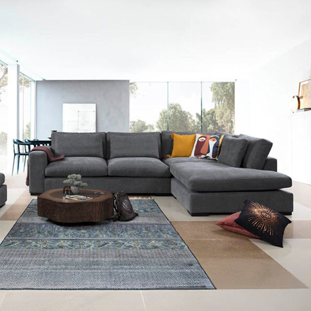 Μοντέρνος γωνιακός καναπές Lagun σε σκούρο γκρι χρώμα, με πλούσια μαξιλάρια και φαρδιά μπράτσα. / Grey