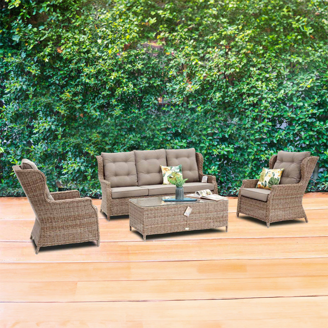 Σετ καθιστικού εξωτερικού χώρου Paros από πλεγμένο ραττάν σε ανοιχτό καφέ με γκριζοκαφέ μαξιλάρια με κουμπιά, που περιλαμβάνει καναπέ τριών θέσεων, δύο πολυθρόνες και τραπεζάκι με γυάλινη επιφάνεια, τοποθετημένο σε ξύλινο πάτωμα με σκούρες αποχρώσεις μπροστά από πυκνό πράσινο φράχτη. / Brown