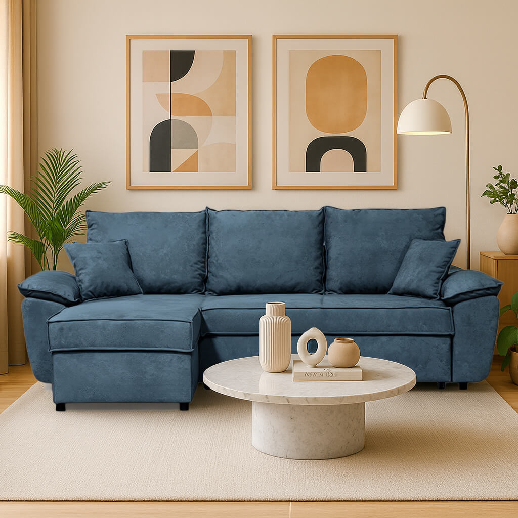 Ένας αναπαυτικός, γωνιακός καναπές σε σκονισμένο μπλε χρώμα με αριστερή γωνία (σεζλόνγκ), σε ένα άνετο, μοντέρνο σαλόνι. Το σκηνικό συμπληρώνεται από ένα στρογγυλό μαρμάρινο τραπεζάκι σαλονιού, δύο κάδρα με αφηρημένη γεωμετρία στον μπεζ τοίχο και ένα καμπυλωτό φωτιστικό δαπέδου. / Blue