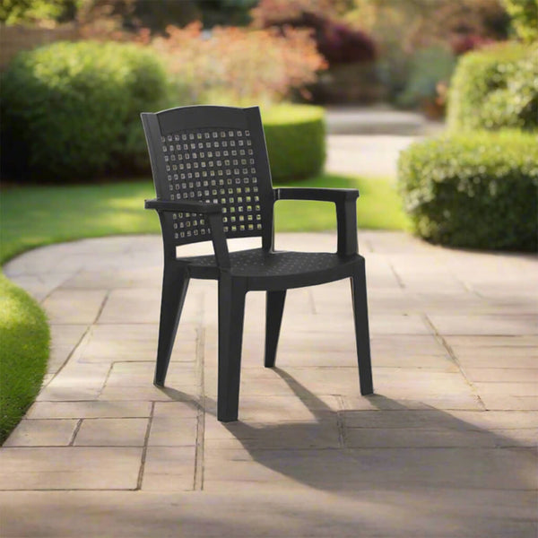 Black plastic outdoor armchair with a perforated back and seat on a stone tile, with neat green shrubs in the background. - Lux Furniture