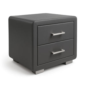 Studio photo of the Kleio nightstand from a side angle on a white background. This modern nightstand with two drawers is fully upholstered in dark grey faux leather and features rounded corners, recessed drawer fronts with handles in a satin silver finish, and two solid base-feet with a matching metal finish.