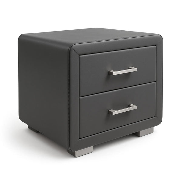 Studio photo of the Kleio nightstand from a side angle on a white background. This modern nightstand with two drawers is fully upholstered in dark grey faux leather and features rounded corners, recessed drawer fronts with handles in a satin silver finish, and two solid base-feet with a matching metal finish.