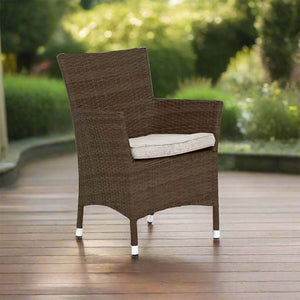 Skiathos brown rattan outdoor armchair with a light beige seat cushion, on a wooden deck in a garden setting. | Lux Furniture