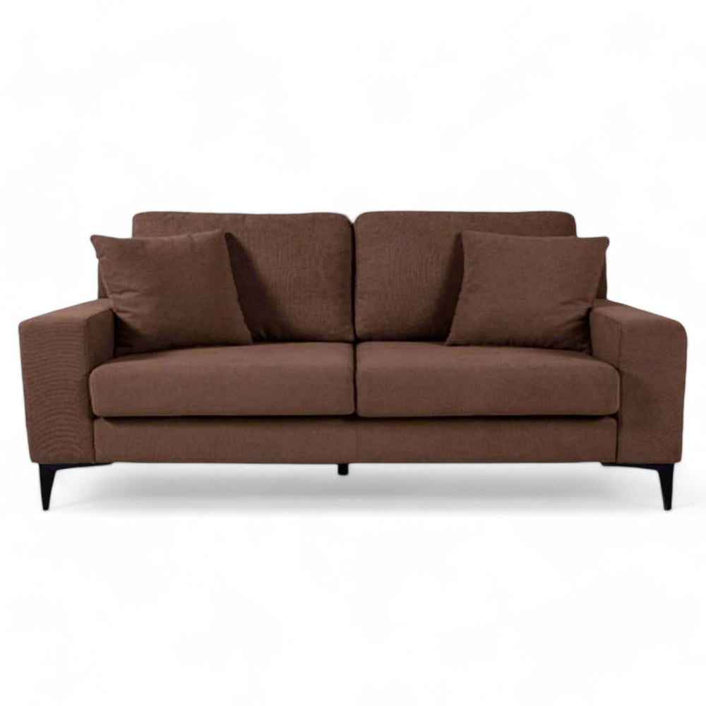 A modern two-seater sofa upholstered in rich chocolate-colored fabric, set in a contemporary living room. It is complemented by a black metal table with a glass top, a large frame with abstract graphic art on the wall and a floor lamp. / Brown